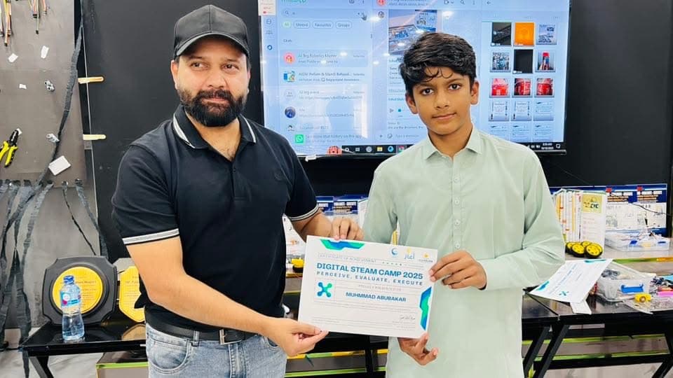 A Digital STEAM Camp 2025 certificate being presented to a student, with robotics parts and kits on the table