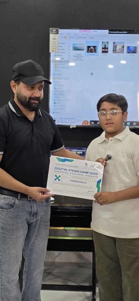 A Digital STEAM Camp 2025 certificate being presented to a student, with robotics kit components visible in the background